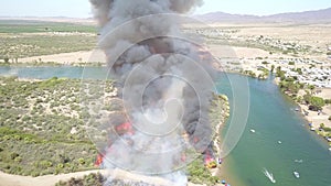 Aerial footage of a brush fire along the silky green waters of the Colorado River surrounded by dry brush and lush green trees