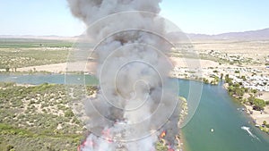 Aerial footage of a brush fire along the silky green waters of the Colorado River surrounded by dry brush and lush green trees