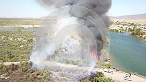 Aerial footage of a brush fire along the silky green waters of the Colorado River surrounded by dry brush and lush green trees