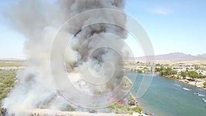 Aerial footage of a brush fire along the silky green waters of the Colorado River surrounded by dry brush and lush green trees