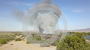 Aerial footage of a brush fire along the silky green waters of the Colorado River surrounded by dry brush and lush green trees