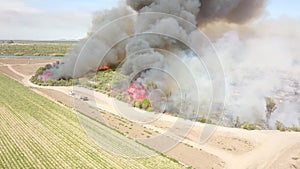 Aerial footage of a brush fire along the silky green waters of the Colorado River surrounded by dry brush and lush green trees