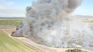 Aerial footage of a brush fire along the silky green waters of the Colorado River surrounded by dry brush and lush green trees