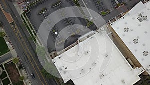 Aerial footage of buildings, cars and trucks driving on the street with parked cars in parking lots and lush green trees, grass