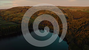 Aerial footage of calm still lake and tall trees during golden sunset in England