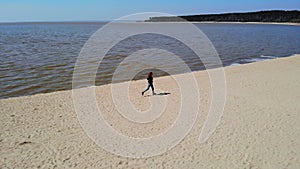 Aerial footage from a drone of a young woman running along a sandy beach near the sea
