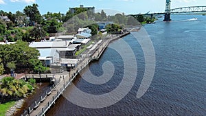 aerial footage flying along the Wilmington Riverwalk and Cape Fear river with Cape Fear Memorial Bridge, boats, lush green trees