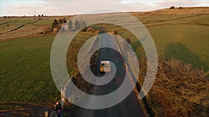 Aerial footage following a vehicle with a dog in the back. Narrow farmland road