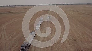 aerial footage of green combine harvesting barley and semi trucks in north dakota in summertime