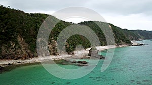 Aerial footage of Kayo Beach with huge rock and turquoise water in Okinawa.