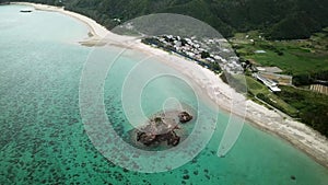 Aerial footage of Kayo Beach with huge rock and turquoise water in Okinawa.