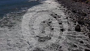 Aerial footage of the majestic waves crashing into the rocks on the beach along the cliffs covered in lush green trees