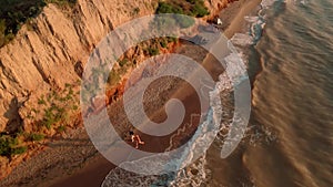 aerial footage of men running at early morning outdoor along sea shore under clay canyon on sea coast. active leisure