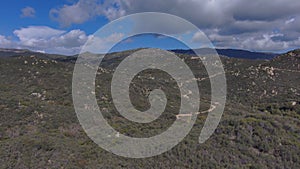 Aerial footage of miles of majestic mountain ranges covered with lush green trees, grass and plants with a gorgeous blue sky