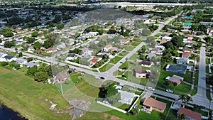 aerial footage of a residential neighborhood with homes surrounded by lush green trees and grass, cars on the street and blue sky