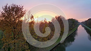 Aerial footage shot by a drone of a Beautiful sunset over a river with green bushes and color rich sky