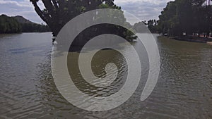 Aerial footage of the silky green rippling waters of Lake Evans surrounded by lush green trees, and plants with powerful clouds