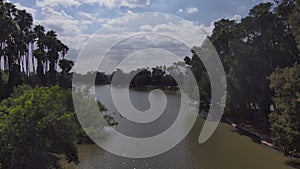 Aerial footage of the silky green rippling waters of Lake Evans surrounded by lush green trees, and plants with powerful clouds