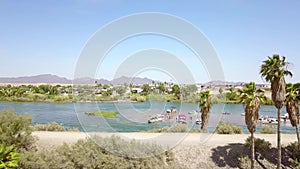 Aerial footage of the silky green waters of the Colorado River with people riding jet skis and lush green trees and plants