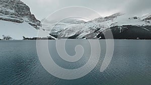 Aerial footage of the surface of Bow Lake with snow-capped mountains in Alberta, Canada