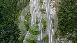 Aerial footage of a twisty asphalt mountain roads with green trees on the cliffs