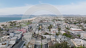 Aerial footage of urban neighbourhood and sand beach on ocean coast. Mountain ridge in background. Los Angeles