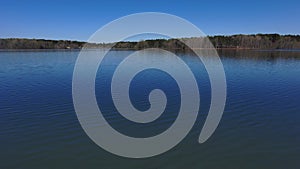 Aerial footage of the vast rippling blue waters of the lake surrounded by lush green trees and plants