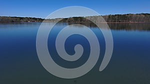 Aerial footage of the vast rippling blue waters of the lake surrounded by lush green trees and plants