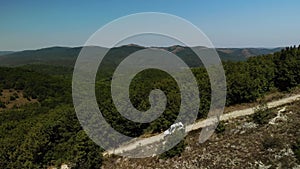 Aerial footage of white SUV going down steep mountain. The white jeep drives through the mountains, making its way to