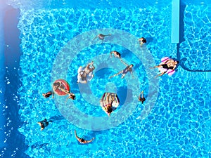Aerial of friends having party in swimming pool with inflatable flamingo, swan, mattress. Happy young people relax at
