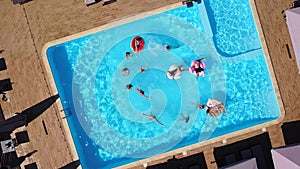 Aerial of friends having party in swimming pool with inflatable flamingo, swan, mattress, ring. Happy young people