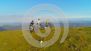 AERIAL: Friends pedalling electric bikes up a grassy hill on a sunny afternoon.