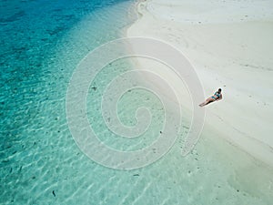 AERIAL: Girl in bikini lying on the sandy beach and suntanning in Cook Islands.