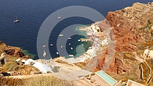 Aerial of the Greek Amoudi Bay with boats by its coastline surrounded by volcanic cliffs