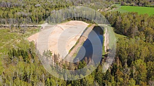 Aerial high angle orbiting shot of an opencast sand, gravel mine quarry with water pond and surrounded by forest
