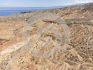 Aerial high angle view of the eroded landscape of Skazka Canyon in Kyrgyzstan with Lake Issyk-Kul in background