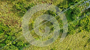 Aerial high voltage steel power pylons in green field countryside. Flight over power transmission lines. Electric tower