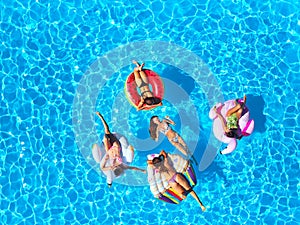 Aerial of hot pretty girls in bikini swimming in pool on floaties. Top view from above. Attractive fitted women in