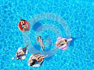 Aerial of hot pretty girls in bikini swimming in pool on floaties. Top view from above. Attractive fitted women in