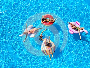 Aerial of hot pretty girls in bikini swimming in pool on floaties. Top view from above. Attractive fitted women in