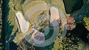 aerial image of a golf field course with a flag and hole and some sand and water pools with beautiful grass