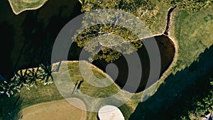 aerial image of a golf field course with a flag and hole and some sand and water pools with beautiful grass