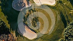 aerial image of a golf field course with a flag and hole and some sand and water pools with beautiful grass