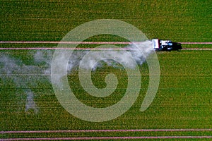 Aerial image of tractor spraying pesticides on green oat field shoot from drone