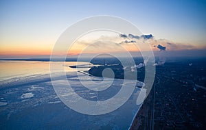 Aerial of industrial plant on the coast of a frozen Sea of Azov in Mariupol. Top view of the factory, smoke rising from