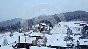 Aerial of inhabited locality in the mountains on winter. Mountain village buildings and houses on snowy hill slopes