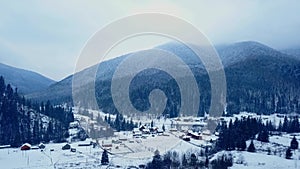 Aerial of inhabited locality in the mountains on winter. Mountain village buildings and houses on snowy hill slopes