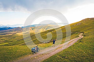 Aerial inspirational view excited joyful caucasian male cyclist standing by red touring bicycle looking to scenic mountains