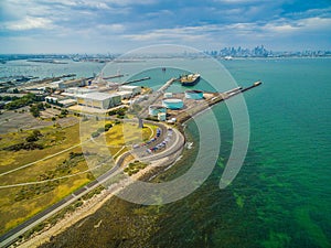 Aerial landscape of parking lot and industrial wharfs near ocean coastline at Williamstown suburb with Melbourne CBD skyline in th