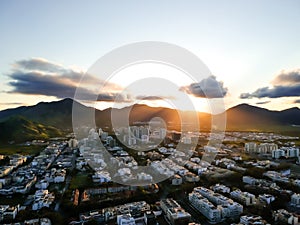 Aerial landscape photo of Recreio dos Bandeirantes beach during sunset, with the sun dipping behind the mountains and